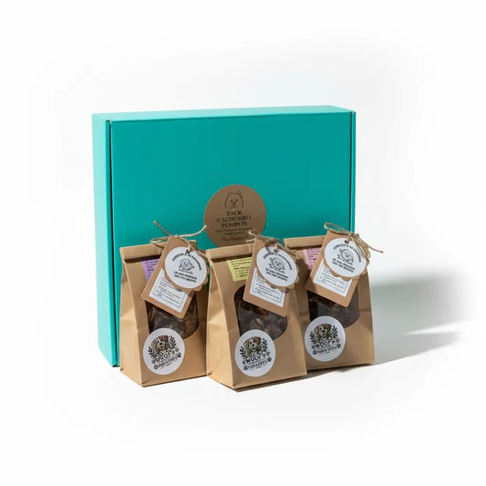 Pack Cachorro Pompón con caja turquesa cerrada y 5 bolsitas de snacks naturales con etiquetas colgantes redondas de Woof Natural dispuestas al frente, presentación completa del producto