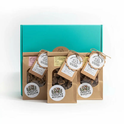 Pack Cachorro Pompón vista frontal con caja turquesa cerrada y 3 bolsitas de snacks naturales con etiquetas colgantes redondas y cordel de yute de Woof Natural dispuestas al frente